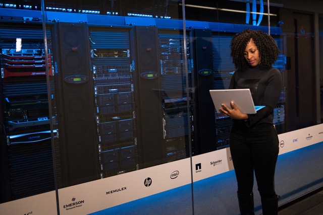 black woman with laptop standing next to a server room